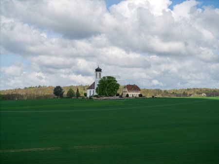 Kleine Kirche mit Friedhof inmitten blühender Obstbäume und Felder, die im Frühjahr mit einer Drohne eingefangen wurden