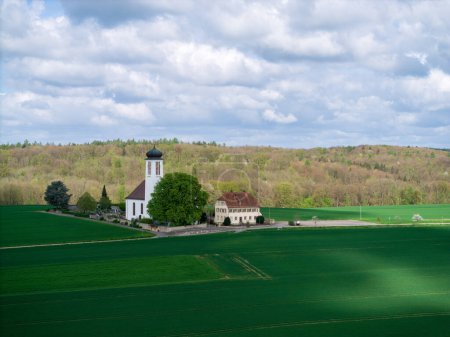 Kleine Kirche mit Friedhof inmitten blühender Obstbäume und Felder, die im Frühjahr mit einer Drohne eingefangen wurden