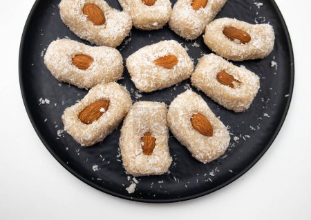 Téléchargez les photos : Bonbons à la noix de coco indienne maison sur plaque noire, fond blanc - en image libre de droit