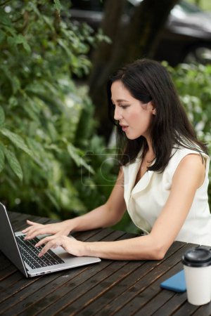 Foto de Young female entrepreneur working on laptop in outdoor cafe - Imagen libre de derechos