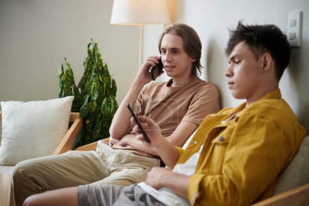 Foto de Young man talking on phone when his friend texting or checking social media - Imagen libre de derechos