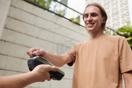 Photo for Smiling student paying for food delivery and swiping credit card - Royalty Free Image