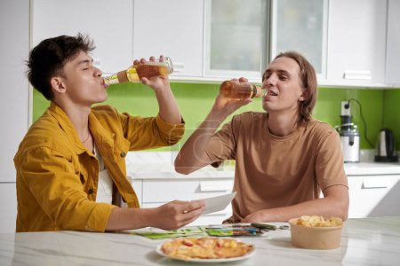 Photo for Young people drinking beer and eating snacks when sitting at kitchen table - Royalty Free Image