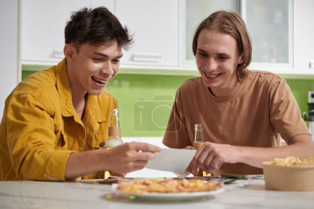 Photo for Happy young men discussing printed photos they made together for contest - Royalty Free Image
