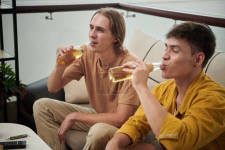 Foto de Young man drinking bottled beer when watching movie or soccer game at home - Imagen libre de derechos