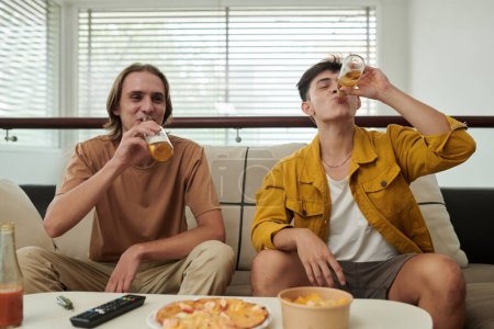 Téléchargez les photos : Young men drinking beer and eating pizza and snacks at home - en image libre de droit