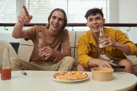 Foto de Joyful young men drinking beer when watching soccer game at home - Imagen libre de derechos