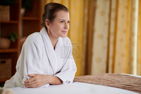Téléchargez les photos : Portrait of smiling mature woman in white bathrobe relaxing after rejuvenating procedure - en image libre de droit