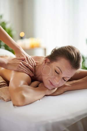 Téléchargez les photos : Mature woman enjoying getting shoulder massage in salon to get rid of stress and anxiety - en image libre de droit