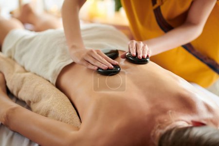 Photo for Masseuse putting warm basalt stones on back of woman - Royalty Free Image
