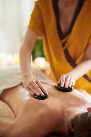 Téléchargez les photos : Cropped image of masseuse giving relaxing stone massage to female client - en image libre de droit