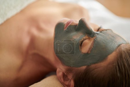Photo for Spa salon client relaxing with rejuvenating and detoxifying clay mask on face - Royalty Free Image