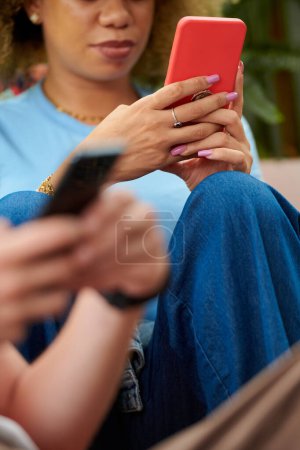 Foto de Young woman with long nails texting instead of talking to friends at party - Imagen libre de derechos