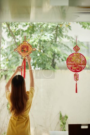 Foto de Hands of woman hanging round pedant on wall to decorate house for Lunar festival with happy new year inscription - Imagen libre de derechos