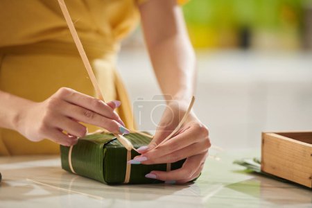 Photo for Closeup image of young woman wrapping traditional rice cake in banana leaves - Royalty Free Image