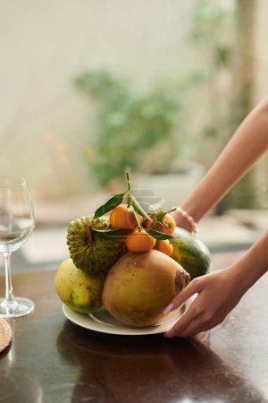 Téléchargez les photos : Hands of woman putting plate with fresh fruits on dinner table - en image libre de droit