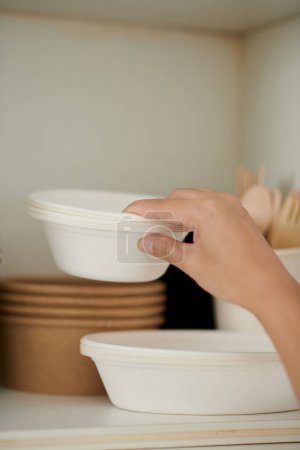 Foto de Closeup image of woman taking disposable bowls out of kitchen cabinet - Imagen libre de derechos
