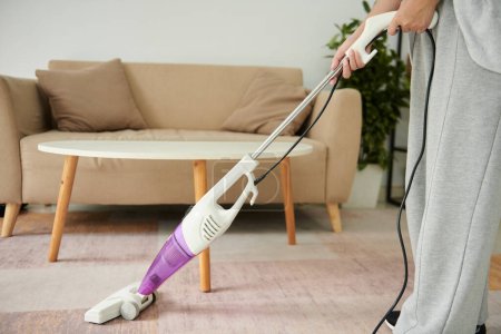 Téléchargez les photos : Cropped image of woman vacuum cleaning carpet in living room - en image libre de droit