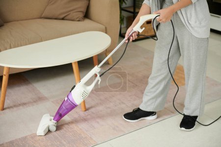 Téléchargez les photos : Housewife in loungewear vacuum cleaning floor in apartment - en image libre de droit