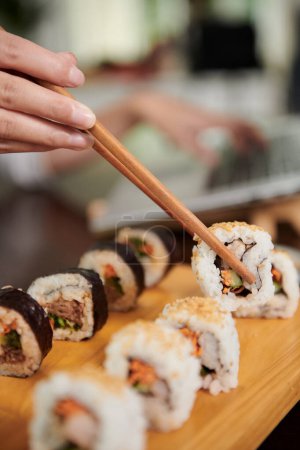 Photo for Hand of woman eating delicious homemade sushi with chopsticks - Royalty Free Image