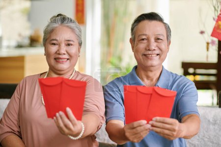 Foto de Portrait of happy elderly couple showing red lucky money envelopes for Lunar New Year Celebration - Imagen libre de derechos