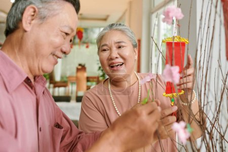 Photo for Joful senior couple decorating peach tree at home for Tet celebration - Royalty Free Image
