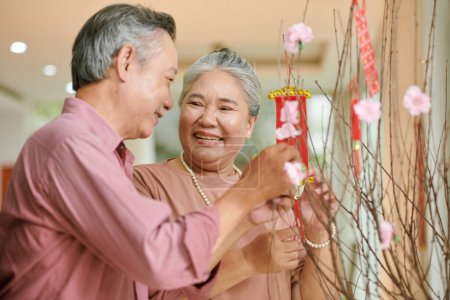 Téléchargez les photos : Senior man and woman decoraing peach tree branches for Lunar New Year celebration - en image libre de droit
