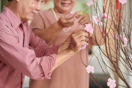 Foto de Senior man decorating branches with artificial pink peach flowers for Tet celebration - Imagen libre de derechos
