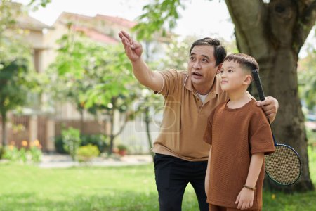 Téléchargez les photos : Grandfather explaining little boy how to play badminton - en image libre de droit