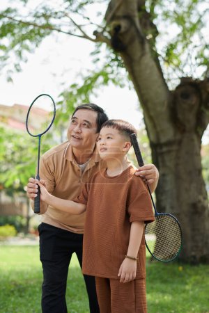 Photo for Grandfather and grandson playing badminton in city park on sunny day - Royalty Free Image