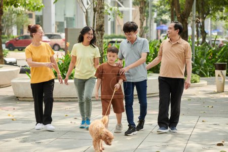 Téléchargez les photos : Family walking in park with small dog on sunny day - en image libre de droit
