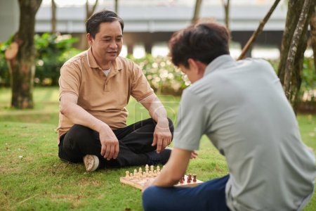 Téléchargez les photos : Senior man and his adult son playing chess in city park - en image libre de droit