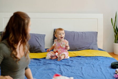 Foto de Young motehr looking at her kid playing on big bed - Imagen libre de derechos