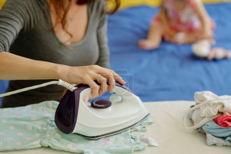 Photo for Closeup image of young woman ironing tidy baby clothes after doing laundry - Royalty Free Image