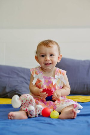 Téléchargez les photos : Adorable happy little girl playing with toys on bed at home - en image libre de droit