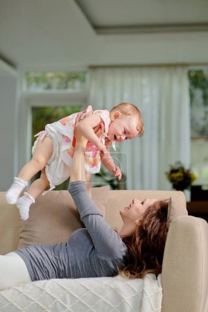 Photo for Young woman lying on sofa and playing with smiling little daughter - Royalty Free Image