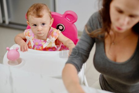Photo for Bored little girl looking at mother washing dishes after feeding - Royalty Free Image