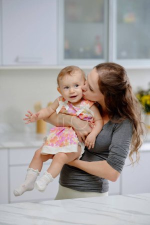 Photo for Joyful young mother kissing baby girl on cheeck - Royalty Free Image