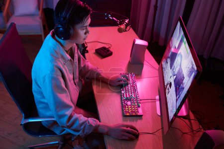 Téléchargez les photos : Serious teenage boy playing game on computer at home - en image libre de droit