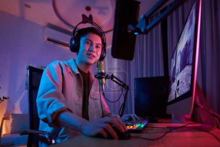 Téléchargez les photos : Positive teenage videogamer playing computer game in neon bedroom at night - en image libre de droit