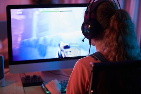 Photo for Girl in headset playing first person shooter, view over shoulder - Royalty Free Image