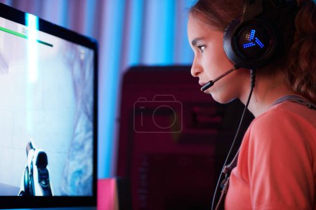 Téléchargez les photos : Serious teenage girl in headset with microphone attempting to defeat enemy in videogame - en image libre de droit