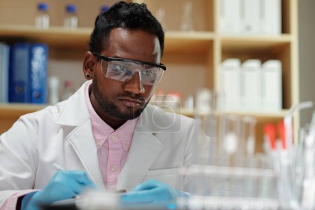 Téléchargez les photos : Serious researcher in goggles checking reagents on laboratory table - en image libre de droit