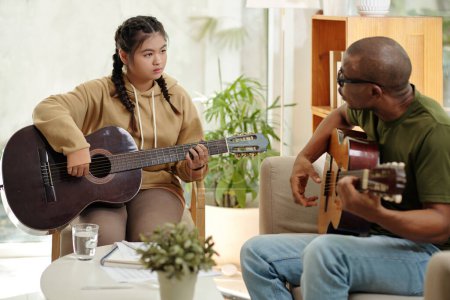 Téléchargez les photos : Confused teenage girl looking at teacher explaining how to play guitar - en image libre de droit