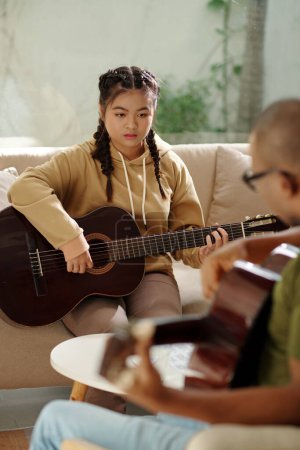 Foto de Serious girl looking at hands of her teacher playing guitar - Imagen libre de derechos