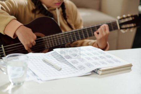 Téléchargez les photos : Closeup image of teenge girl folloving music notes in textbook when playing guitar - en image libre de droit