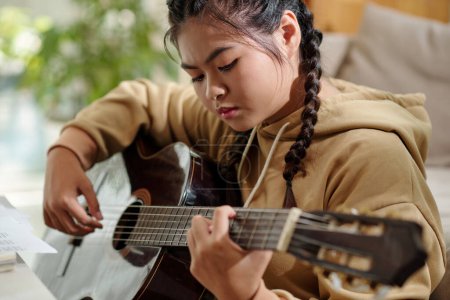 Foto de Portrait of serious teenage girl playing guitar alone learning new song - Imagen libre de derechos