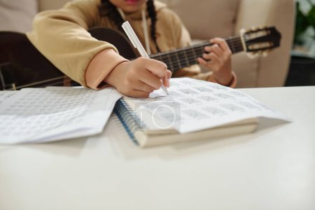 Photo for Girl taking notes in textbook when playing guitar at home - Royalty Free Image