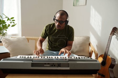 Téléchargez les photos : Musician in headphones enjoying playing synthesizer at home - en image libre de droit