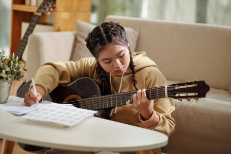 Foto de Teenage girl practicing new chords when playing guitar at home - Imagen libre de derechos